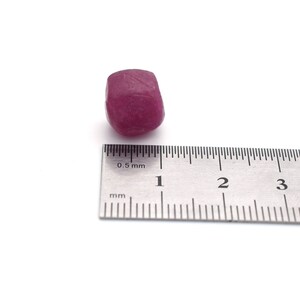 Op de afbeelding: Een dieproze edelsteen met een diameter van ongeveer 1 cm, naast een liniaal die in millimeters is gemarkeerd.