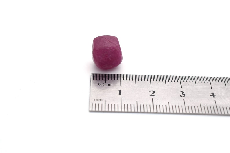 Op de afbeelding: Een dieproze edelsteen met een diameter van ongeveer 1 cm, naast een liniaal die in millimeters is gemarkeerd.