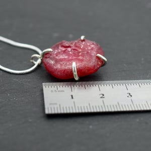 K&ouml;nnte beinhalten: Ein roter Glasanh&auml;nger mit silbernen Akzenten h&auml;ngt an einer silbernen Kette. Der Anh&auml;nger hat einen Durchmesser von etwa 2,5 cm und wird an einem Lineal gemessen.