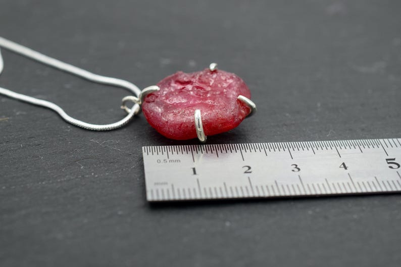 K&ouml;nnte beinhalten: Ein roter Glasanh&auml;nger mit silbernen Akzenten h&auml;ngt an einer silbernen Kette. Der Anh&auml;nger hat einen Durchmesser von etwa 2,5 cm und wird an einem Lineal gemessen.