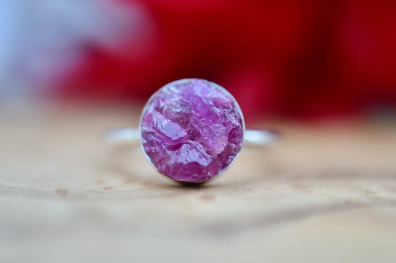 May include: A silver ring with a round, pink, raw gemstone set in the center.