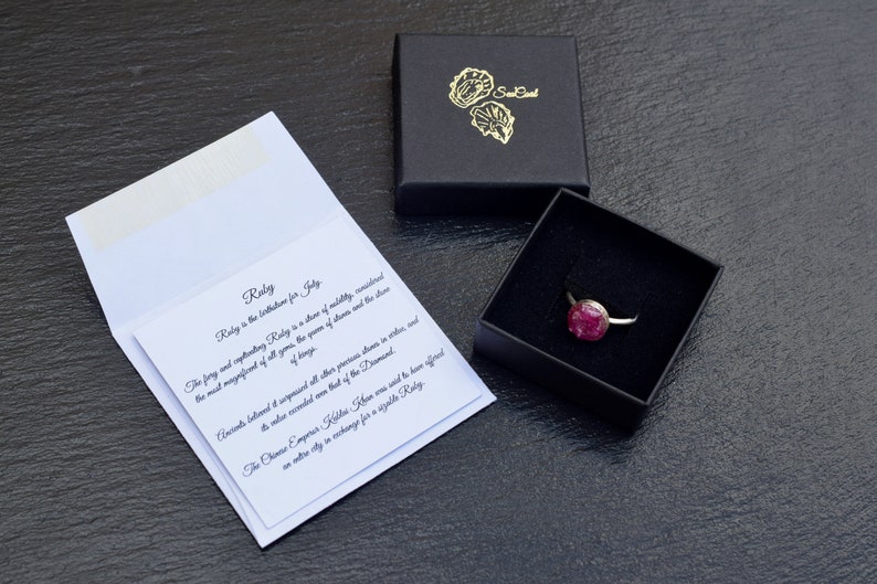 May include: A red ruby ring in a black ring box with a white card that reads "Ruby is the birthstone for July. The fiery and captivating Ruby is a stone of nobility, considered the most magnificent of all gems. The queen of gems and the stone of kings. Accounts tell us it surpassed all other precious stones in value and exceeded even that of the Diamond. The Chinese Emperor Kublai Khan was said to have offered an entire city in exchange for a single Ruby."