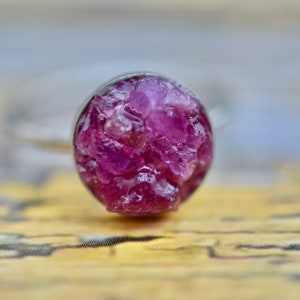 May include: A silver ring with a round, pink gemstone setting. The gemstone is made of many small, faceted crystals.