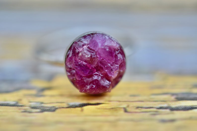May include: A silver ring with a round, pink gemstone setting. The gemstone is made of many small, faceted crystals.