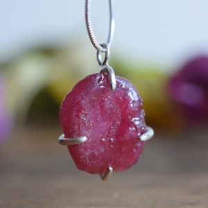 May include: A silver chain necklace with a pink, faceted gemstone pendant. The pendant is held in place by silver wire.