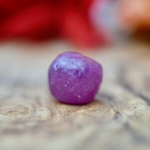 Op de afbeelding: Een enkele, gefacetteerde, paarse edelsteen. De edelsteen is rond en heeft een glad, gepolijst oppervlak.