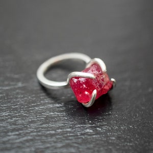 May include: A silver ring with a large, faceted, red gemstone set in a simple, modern design.
