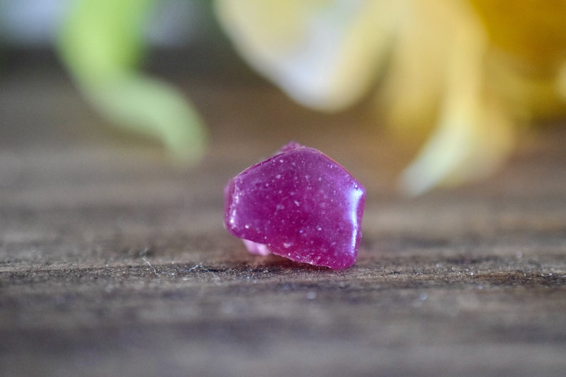 Op de afbeelding: Een diep roze, gefacetteerde edelsteen met een ruw, getextureerd oppervlak. De edelsteen ligt op een houten oppervlak.