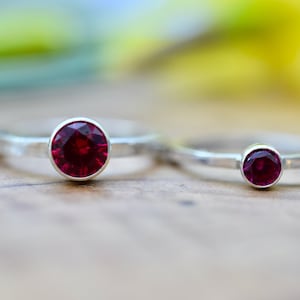 May include: Two silver rings with red gemstone settings. The rings are on a wooden surface.