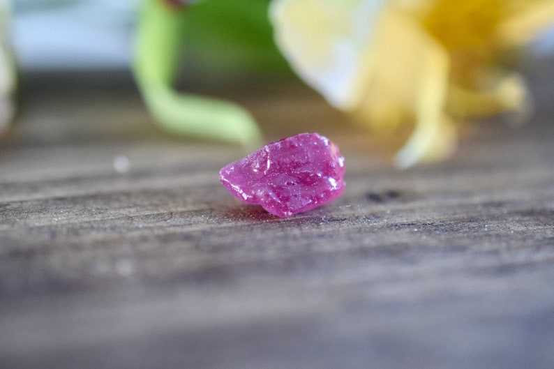 Op de afbeelding: Een kleine, ruwe, roze robijn edelsteen op een houten oppervlak.