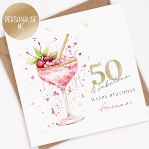 May include: A birthday card with a watercolor illustration of a pink cocktail with cherries and a gold straw. The card says "50 & fabulous" and "Happy Birthday Ariana". A gold sticker says "Personalise Me".