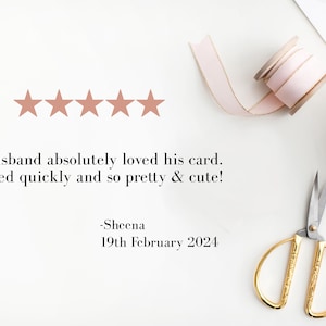 May include: A flat lay featuring a customer review with five star ratings. The text reads, "My husband absolutely loved his card." Gold scissors, a pink ribbon, and a small gift box are also visible.
