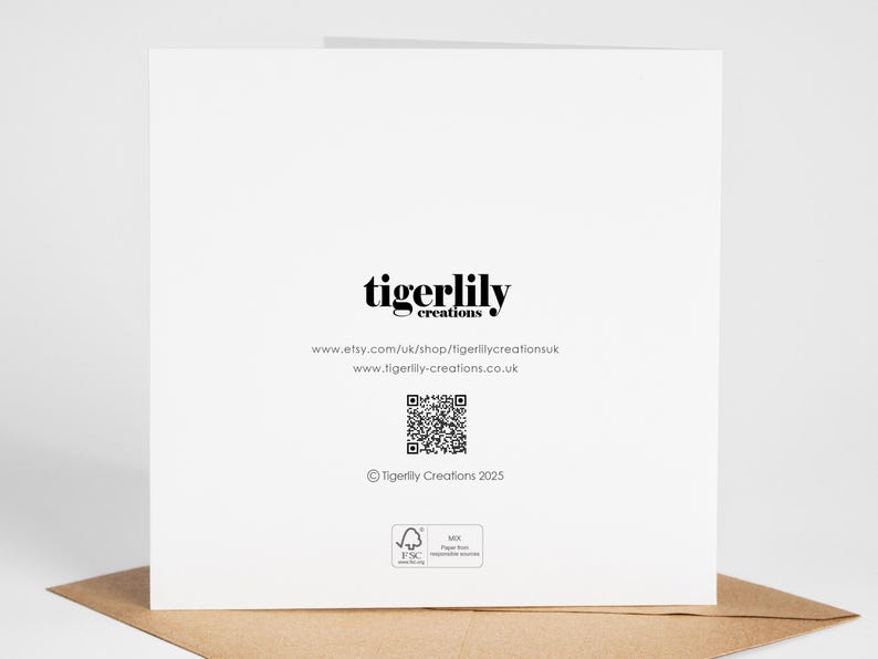 May include: A white greeting card with the text "tigerlily creations" in black. Below the text are website addresses and a QR code. The card is on a brown envelope.
