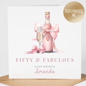 May include: Pink birthday card with a champagne bottle and glass, decorated with a pink bow and a heart charm. The card says "Fifty & Fabulous" and "Happy Birthday Amanda".