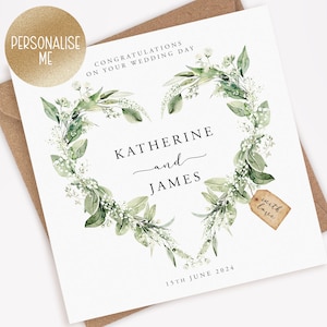 May include: A white wedding card featuring a green leafy heart wreath, the names Katherine and James, and the date 15th June 2024. The card has a small brown tag with the words "with love" written on it.