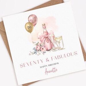 May include: A birthday card with a champagne bottle, two glasses, and balloons. The card reads "SEVENTY & FABULOUS" and "HAPPY BIRTHDAY Annette". The design includes pink flowers and a pink bow.