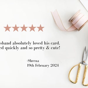 May include: Five gold stars with a review that reads "My husband absolutely loved his card. Shipped quickly and so pretty & cute! -Sheena 19th February 2024". The image also shows a pink ribbon, a spool of pink ribbon, a pair of gold scissors, and a white gift box with a pink ribbon.