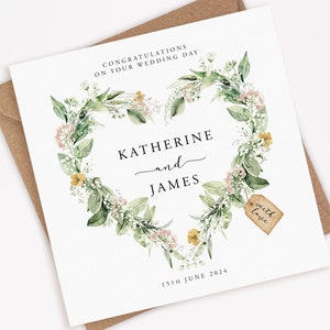 May include: A square wedding card with a floral heart wreath design. The card features the names "Katherine and James" and the date "15th June 2024". A small tag reads "with love". The card is on a brown envelope.