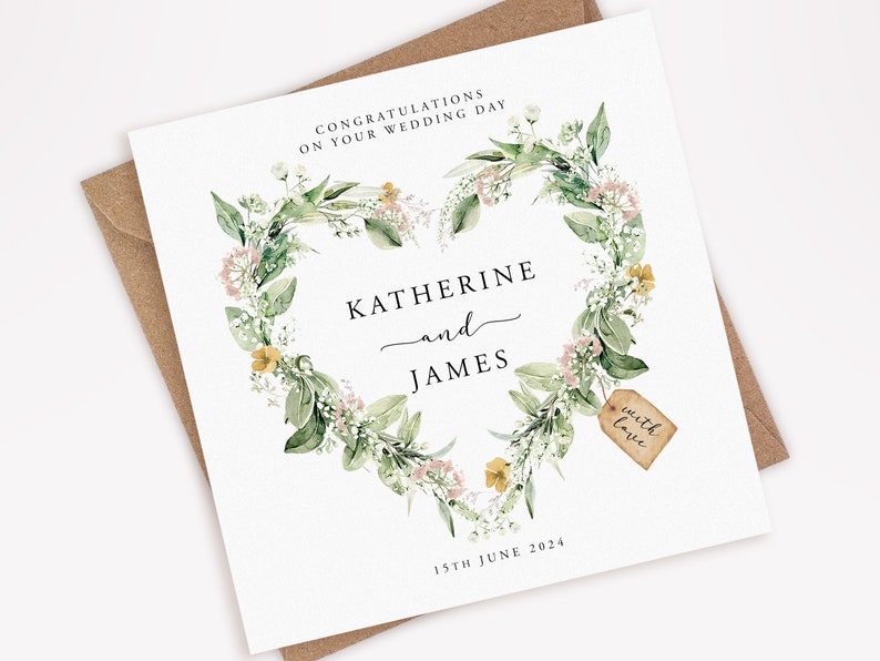 May include: A square wedding card with a floral heart wreath design. The card features the names "Katherine and James" and the date "15th June 2024". A small tag reads "with love". The card is on a brown envelope.