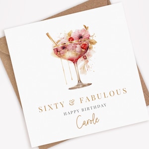 Peut inclure: Une carte blanche avec une inscription dor&eacute;e qui dit "Soixante & Fabuleux Joyeux Anniversaire Carole". La carte pr&eacute;sente une illustration aquarelle d'un cocktail rose avec une paille dor&eacute;e et des fleurs roses.