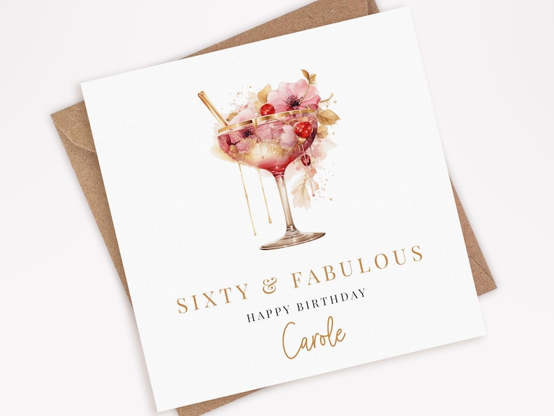 Peut inclure: Une carte blanche avec une inscription dor&eacute;e qui dit "Soixante & Fabuleux Joyeux Anniversaire Carole". La carte pr&eacute;sente une illustration aquarelle d'un cocktail rose avec une paille dor&eacute;e et des fleurs roses.