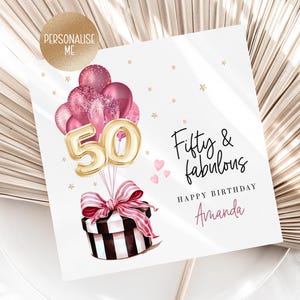 Puede incluir: Tarjeta de cumplea&ntilde;os con el texto "Fifty & fabulous" y "Happy Birthday Amanda". La tarjeta presenta una caja de regalo con un lazo rosa, globos y el n&uacute;mero "50" en dorado. Corazones rosas y estrellas doradas decoran la tarjeta.