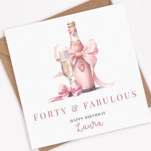 Puede incluir: Tarjeta de felicitaci&oacute;n blanca con una ilustraci&oacute;n en acuarela de una botella y una copa de champ&aacute;n rosas, adornadas con lazos rosas. El texto dice "FORTY & FABULOUS" y "HAPPY BIRTHDAY Laura". Incluye un sobre marr&oacute;n.