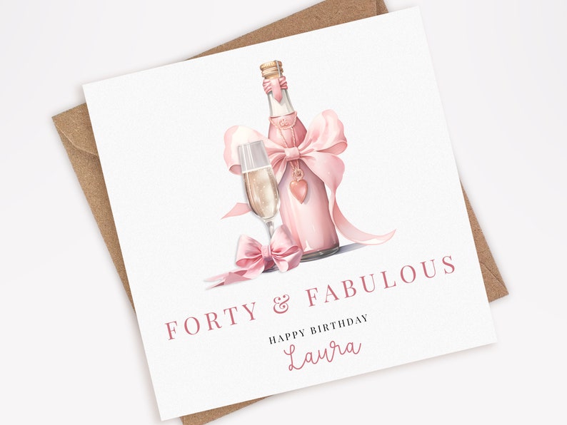 Puede incluir: Tarjeta de felicitaci&oacute;n blanca con una ilustraci&oacute;n en acuarela de una botella y una copa de champ&aacute;n rosas, adornadas con lazos rosas. El texto dice "FORTY & FABULOUS" y "HAPPY BIRTHDAY Laura". Incluye un sobre marr&oacute;n.