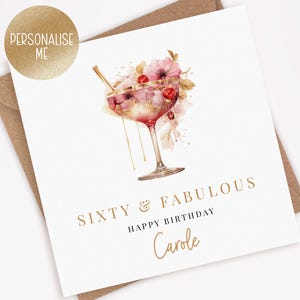 Peut inclure: Une carte blanche avec une inscription dor&eacute;e qui dit "Soixante & Fabuleux Joyeux Anniversaire Carole". La carte pr&eacute;sente une illustration aquarelle d'un cocktail rose avec une paille dor&eacute;e et des fleurs roses.