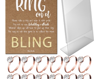 May include: A bridal shower game set with a brown card that reads "Put a Ring on It" and "Bling". Includes a clear acrylic sign holder and rose gold rings with clear gemstones.