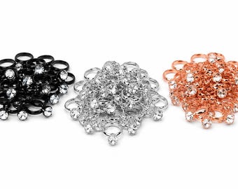 May include: Three decorative brooches in black, silver, and rose gold. Each brooch features a circular design with multiple rings and sparkling clear gemstones. The brooches are arranged on a white background.