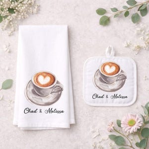 Puede incluir: Un juego de toalla de cocina y agarradera blancos con un diseño de acuarela de una taza de café con arte latte en forma de corazón. Los nombres "Chad & Melissa" están impresos debajo.