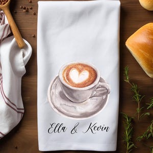 May include: White kitchen towel with a watercolor illustration of a cup of coffee with a heart design in the foam. The text "Ella & Kevin" is printed below the coffee cup.