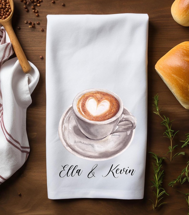 May include: White kitchen towel with a watercolor illustration of a cup of coffee with a heart design in the foam. The text "Ella & Kevin" is printed below the coffee cup.