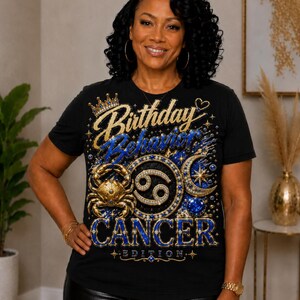 Puede incluir: Una camiseta negra de manga corta con un estampado gráfico que incluye el texto Birthday Behavior y CANCER EDITION. El diseño presenta una corona dorada, un cangrejo dorado, una luna creciente, estrellas y detalles decorativos en azul y oro.