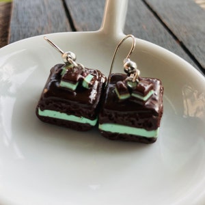 May include: A pair of chocolate and mint-colored earrings shaped like small squares. The earrings are made of polymer clay and have silver hooks.