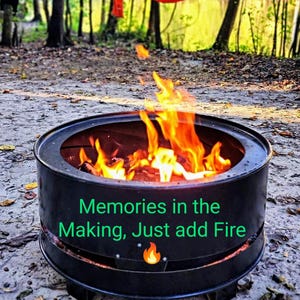 Puede incluir: Un brasero redondo de metal negro con llamas brillantes de color naranja y amarillo ardiendo en su interior. El lateral del brasero presenta el texto verde "Memories in the Making, Just add Fire" junto a un icono de llama naranja.