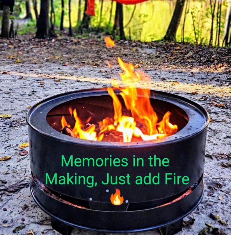Puede incluir: Un brasero redondo de metal negro con llamas brillantes de color naranja y amarillo ardiendo en su interior. El lateral del brasero presenta el texto verde "Memories in the Making, Just add Fire" junto a un icono de llama naranja.