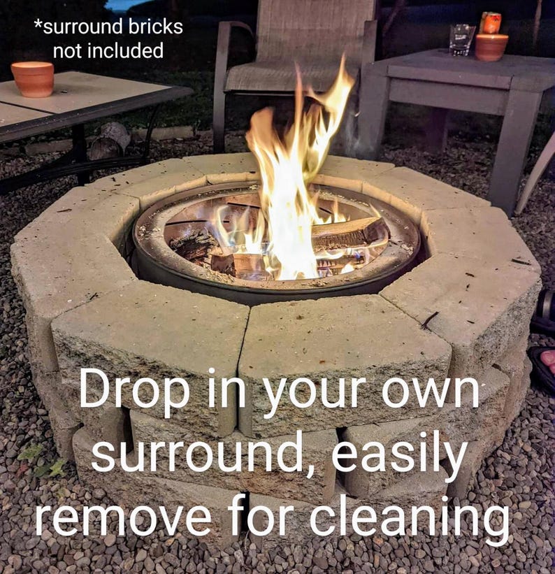 Puede incluir: Un inserto circular de metal para fogata con un fuego de le&ntilde;a encendido en su interior, rodeado por un anillo de bloques de hormig&oacute;n gris claro. El texto en la imagen dice: *surround bricks not included, Drop in your own surround, easily remove for cleaning.