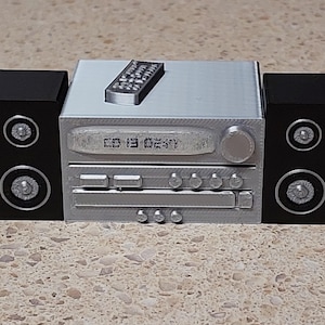 May include: A silver stereo system with two black speakers. The stereo has a digital display showing "CD 13 02:57" and a remote control on top. The speakers have silver speaker cones.