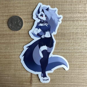 May include: A sticker featuring a gray wolf-like character with long white hair, wearing a black and blue outfit and black boots. The character has red eyes and a black choker with a silver stud. The sticker is on a wooden surface.
