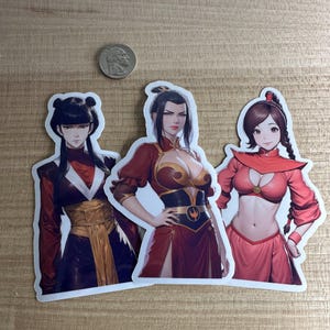 Puede incluir: Tres pegatinas troqueladas con ilustraciones de estilo anime de personajes femeninos con trajes rojos y oscuros. Las pegatinas están sobre una superficie marrón claro, con una moneda para comparar el tamaño.