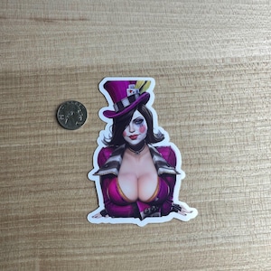 May include: A sticker featuring a stylized illustration of a woman in a purple top hat and jacket. The woman has dark hair, makeup, and a choker. The sticker is on a wooden surface.