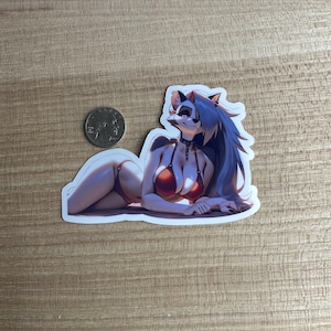 Puede incluir: Una pegatina con un personaje peludo con cabello azul que lleva un top de bikini rojo y una parte inferior de bikini blanca. El personaje está acostado de lado con la cabeza girada hacia un lado.