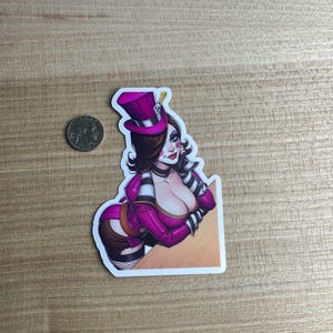 May include: A sticker featuring a cartoon illustration of a woman in a purple outfit and top hat. The woman has dark hair, red lipstick, and a choker. The sticker is on a wooden surface.