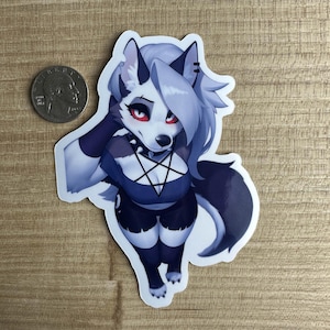 Puede incluir: Una pegatina con un lobo blanco con ojos rojos que lleva un top negro en forma de pentagrama y un collar negro. El lobo tiene un patrón de pelaje blanco y gris y mira al espectador.