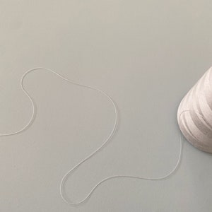 May include: A white thread spool with a white thread trailing off of it on a light gray surface.