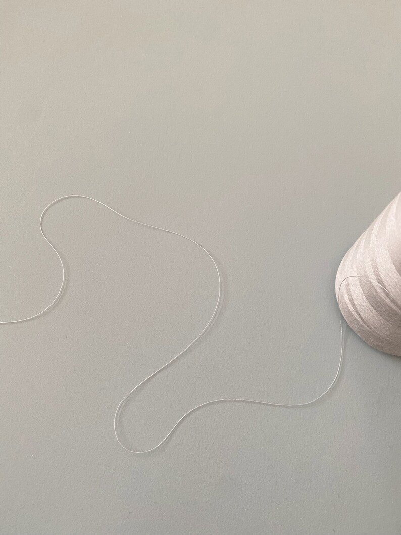 May include: A white thread spool with a white thread trailing off of it on a light gray surface.