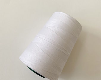 Puede incluir: Una bobina de hilo blanco con un centro de plástico verde.