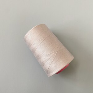 May include: A spool of white thread with a pink plastic bobbin.